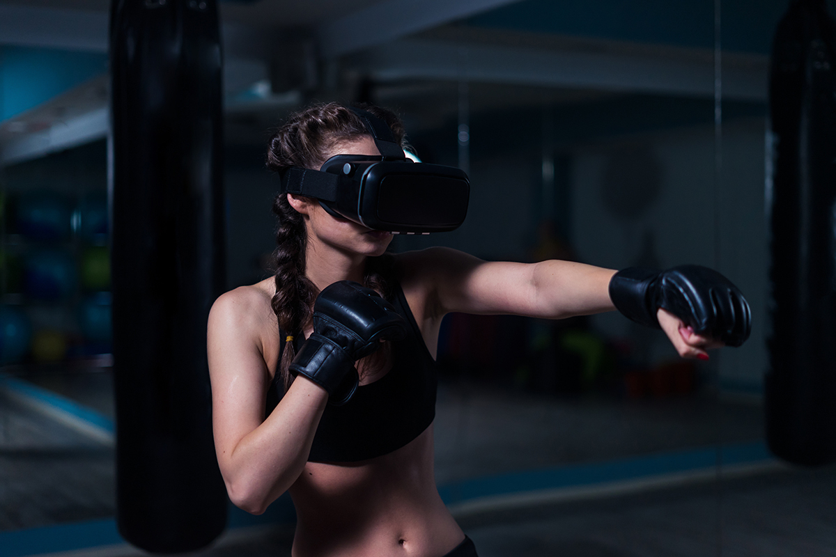 Young fighter boxer fit girl in VR glasses wearing boxing gloves in training. Boxing game in virtual reality 360 degrees. Futuristic gaming in real gym